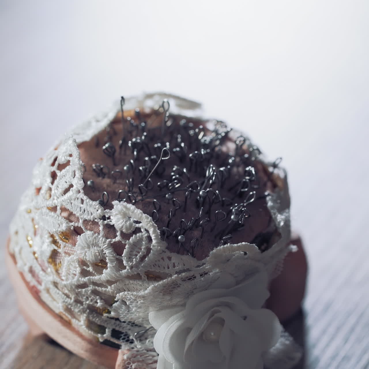 Female hand with beautiful nails taking pins from the white small pincushion. A lot of sewing pins in a sponge for dressmaker on the wooden table. Close-up.