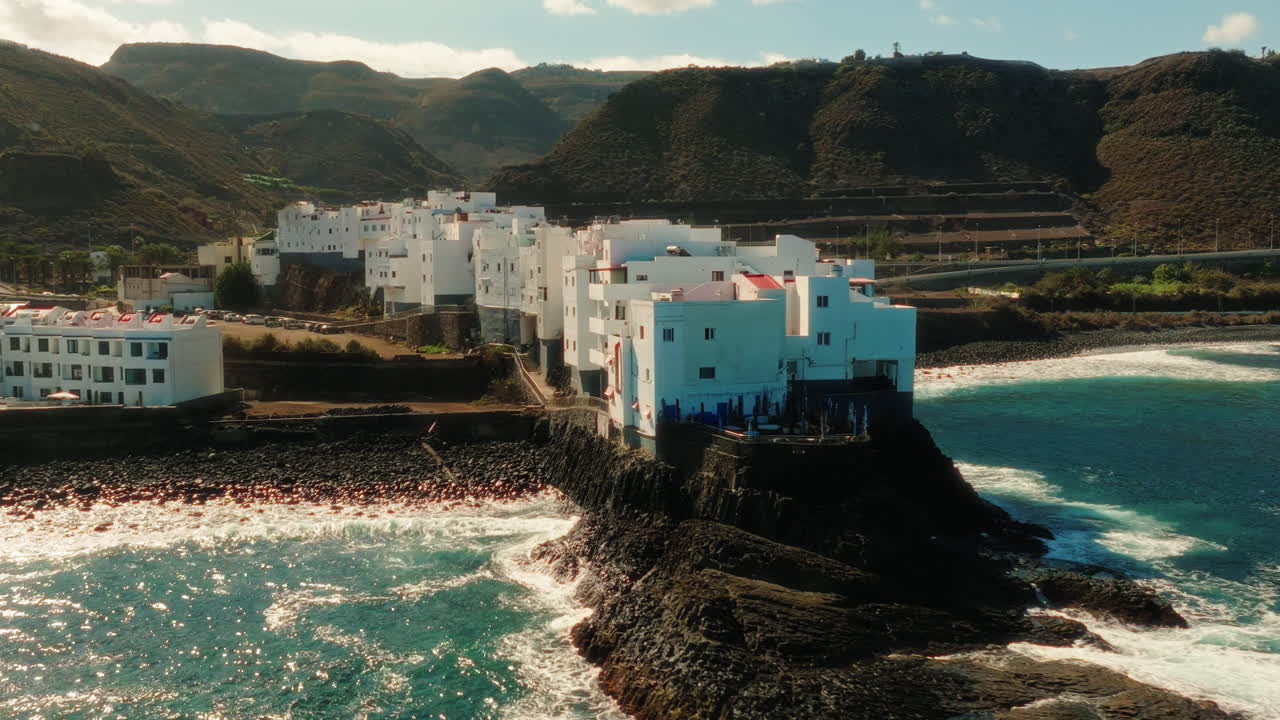 Aerial: Atlantic Ocean, shore and white neighborhood during the day in Gran Canaria, Spain, orbit drone shot