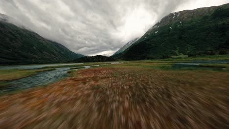 fpv drone flying over alaskan lake with storm clouds and lush green mountain range in the background