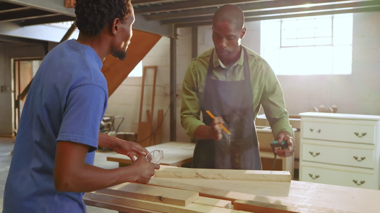 After placing plank, African American mentor and apprentice measuring and marking wood on workbench