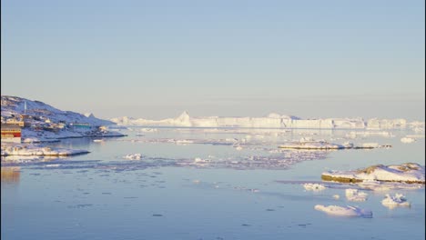 ice, sea and sunlit town on coastline near ilulissat icefjord