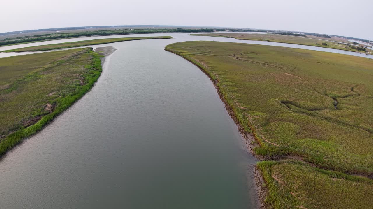 Drone footage showcases a wide river cutting through marshland near Charleston, South Carolina, capturing lush grasses along the water's edge and a tranquil natural landscape from an aerial viewpoint