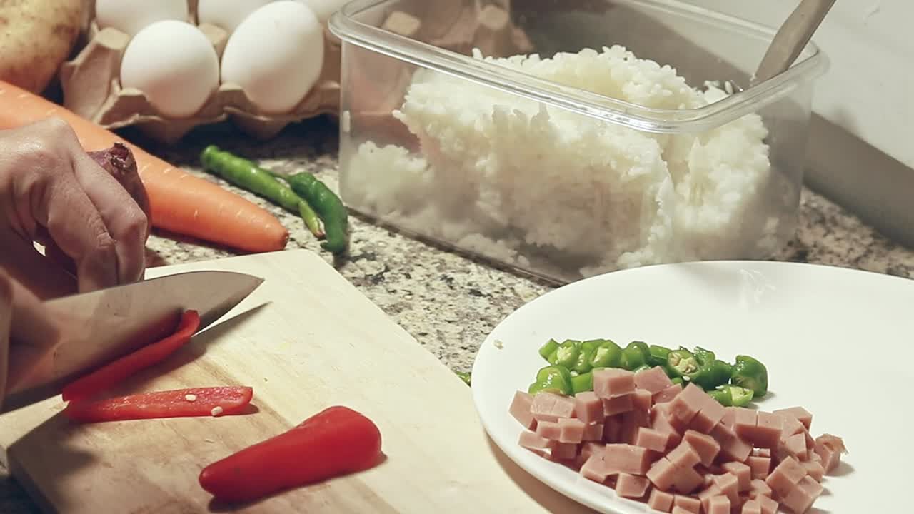 Close up to hands chopping red paprika, preparing the ingredients for cooking fried rice showing a candid daily home life