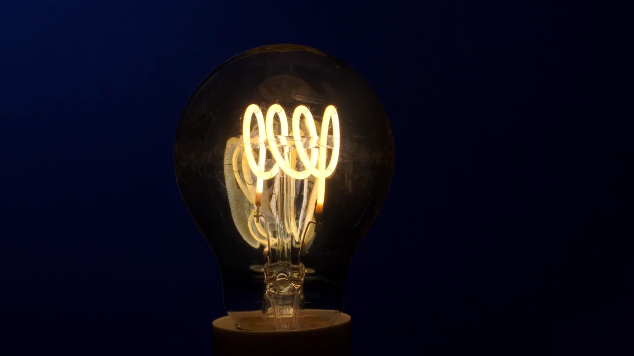LED filament Light bulb switching off on a blue background