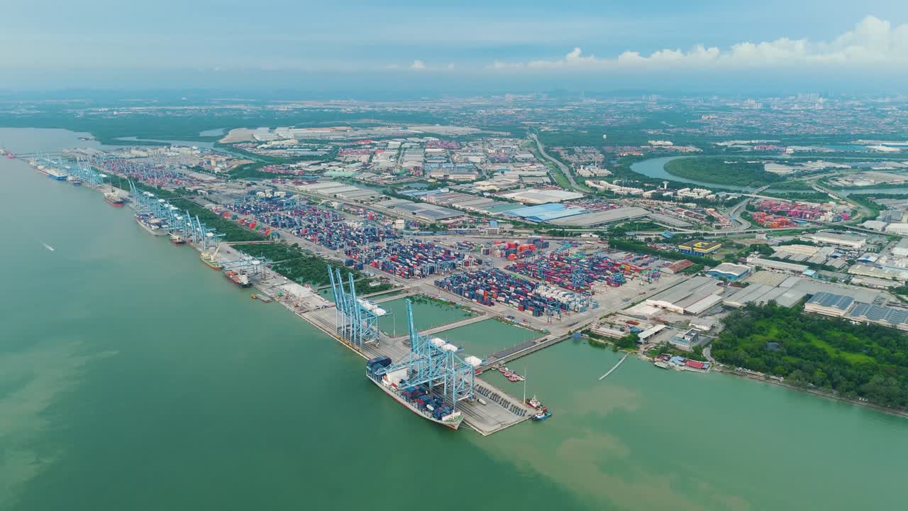 Expansive drone shot of Northport in Klang, Malaysia, revealing container terminals, port infrastructure, and a sprawling cityscape under a partly cloudy sky.