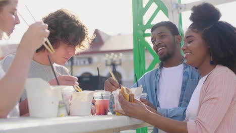 group of cheerful  friends eating street food in the city while laughing and having fun together