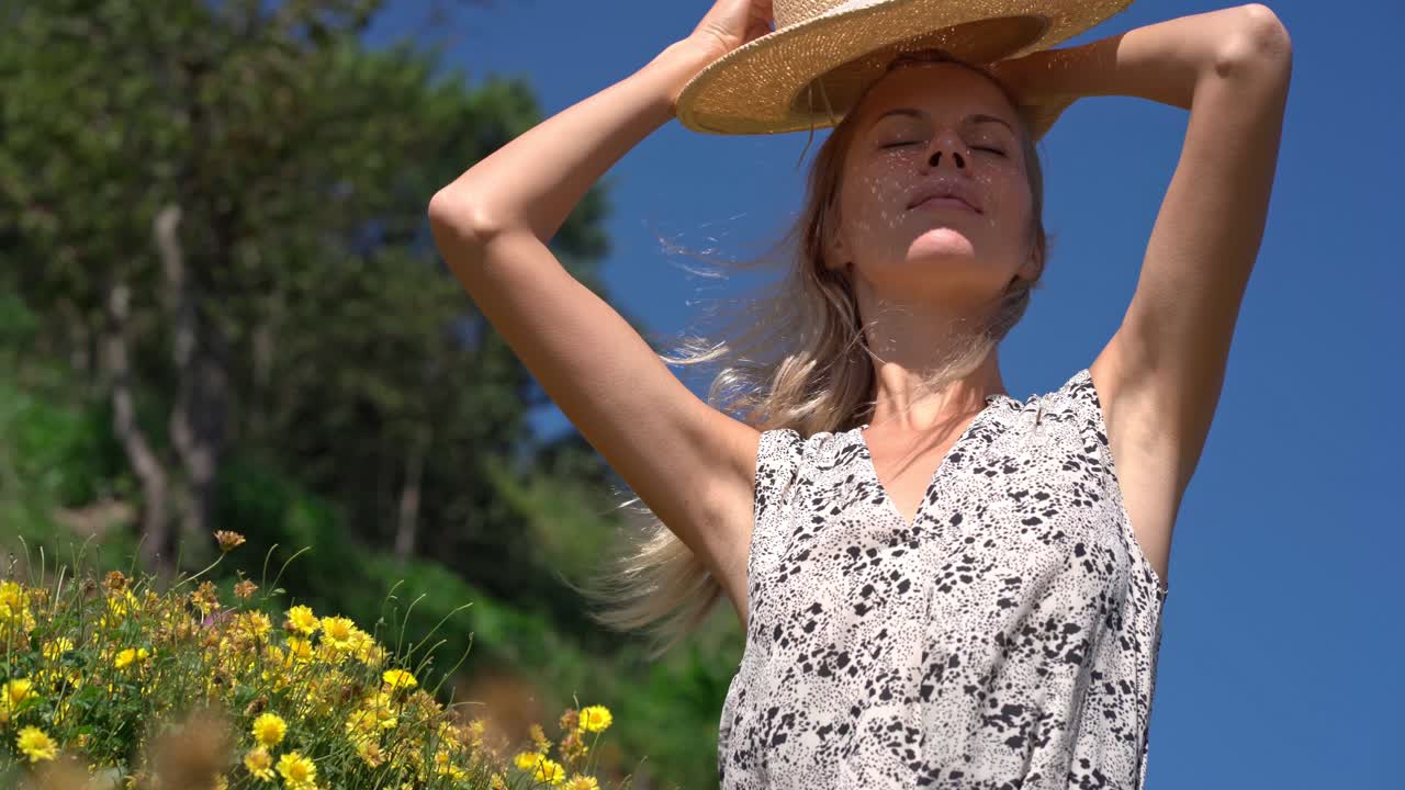 Giovane donna bionda con cappello di paglia che si gode una giornata di sole in un campo fiorito