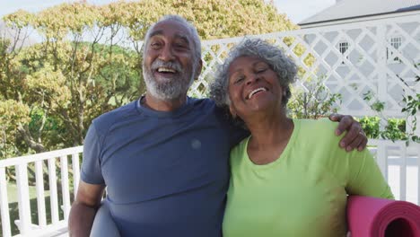 Happy-african-american-senior-couple-holding-yoga-mats-on-patio