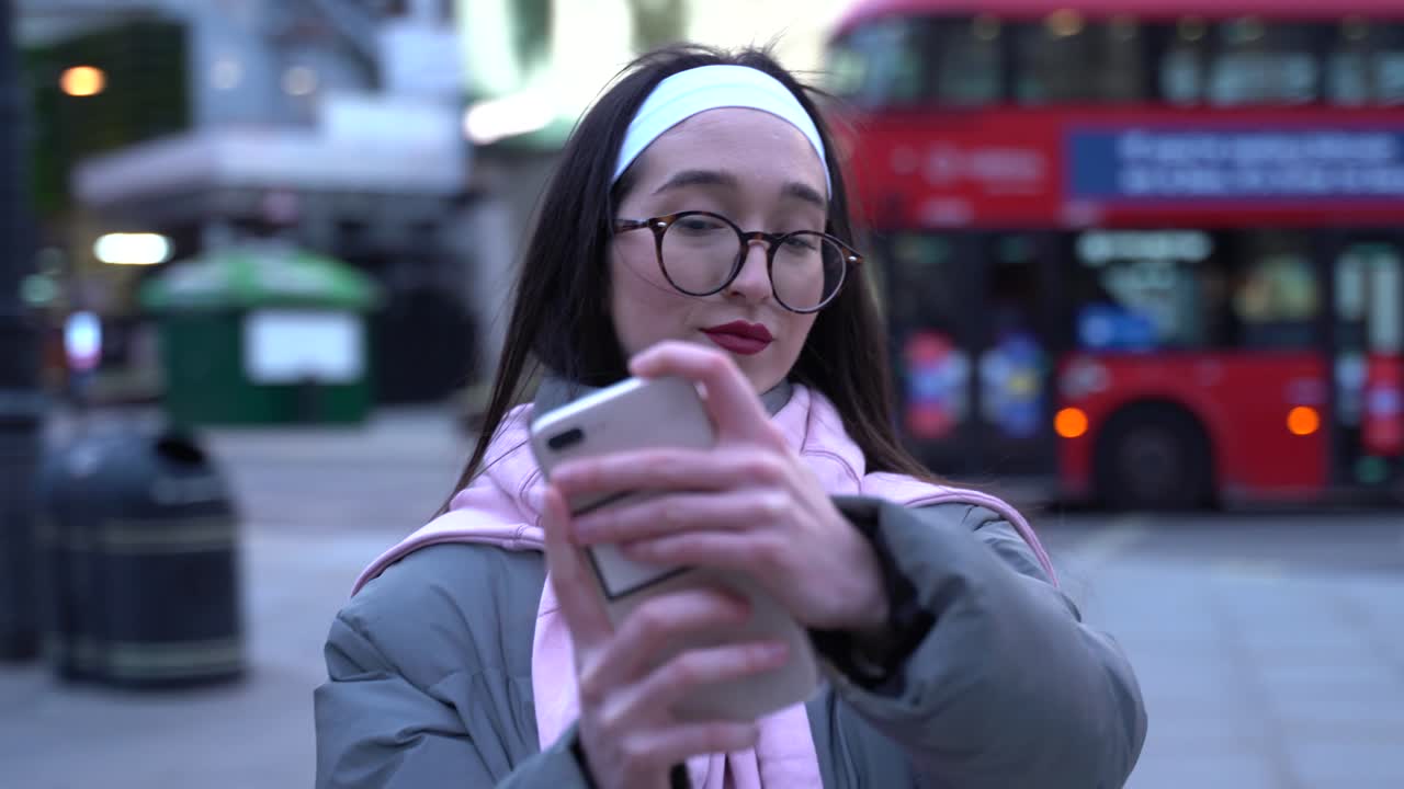 Pretty girl taking a selfie in streets of London with many people around and red double decker busses.