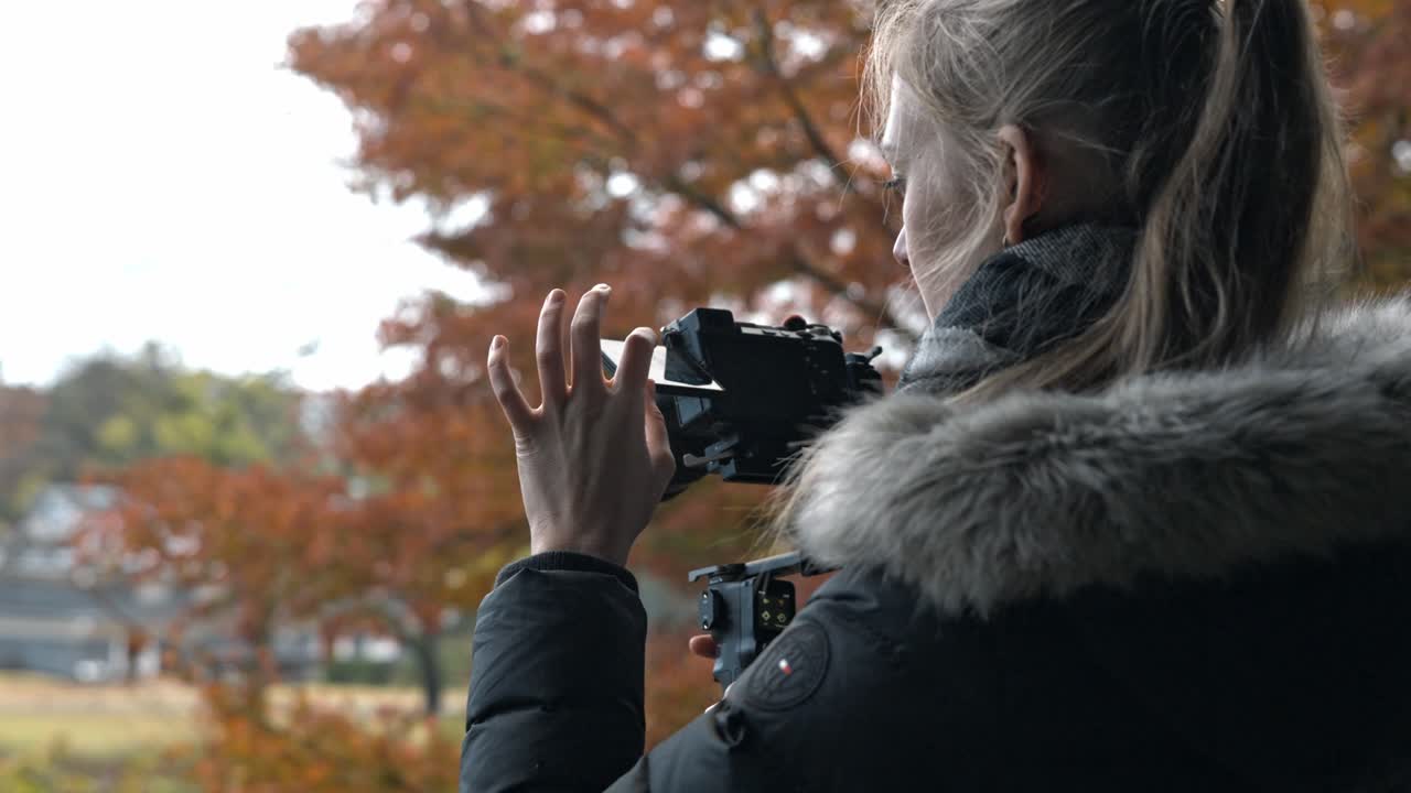 A filmmaker sets up their camera amidst the vibrant autumn foliage in Kanazawa, Japan.