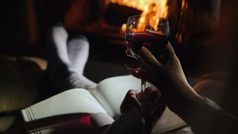 woman sitting by the fireplace with a notebook and a glass of red wine