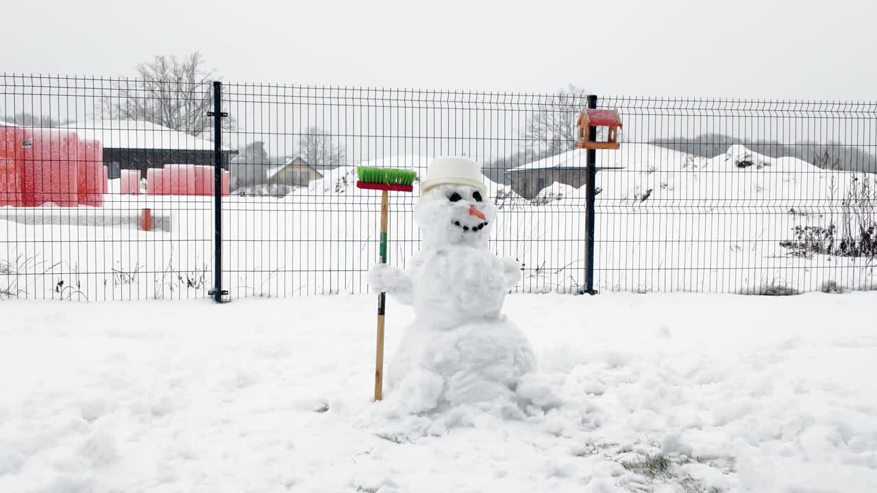 Charming snowman stands in snowy field, holding a colorful broom, exuding a playful winter vibe. Overcast sky enhances serene atmosphere, perfect for festive scenes
