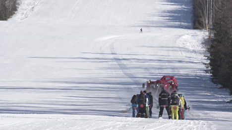 red snow groomer towing a group of skiers uphill a ski slope,czechia