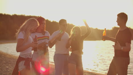 Un-Grupo-De-Estudiantes-Celebra-La-Graduación-Con-Cerveza-En-La-Playa-De-Arena.-Están-Bailando-En-La-Fiesta-Al-Aire-Libre-Al-Atardecer.