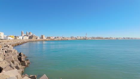 the coastline features angular breakwaters with a panoramic view of a historic city and clear waters