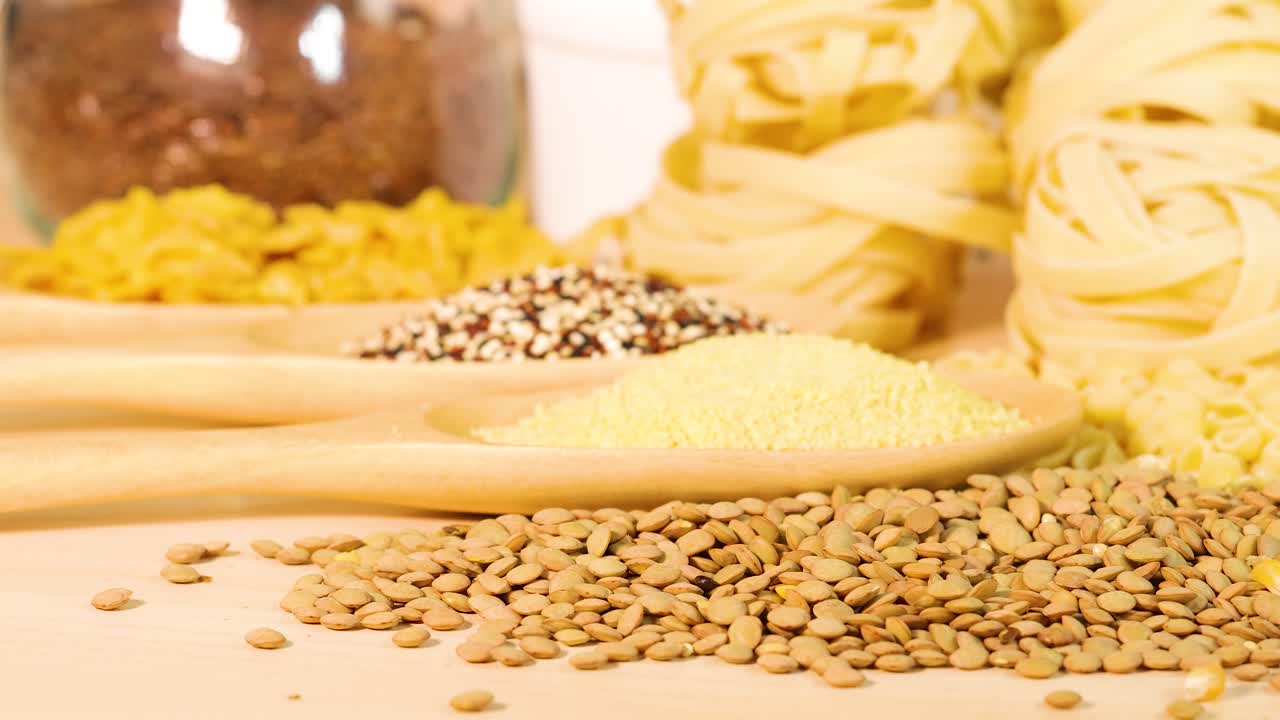 Close-up of various grains and pasta on a wooden surface with soft lighting, highlighting texture and color contrast