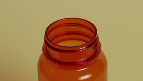 Slow-motion-high-angle-close-up-of-a-pill-bottle-as-a-pill-falls,-hits-the-rim-and-bounces-out