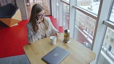 woman working in a modern office, drinking tea and talking on phone