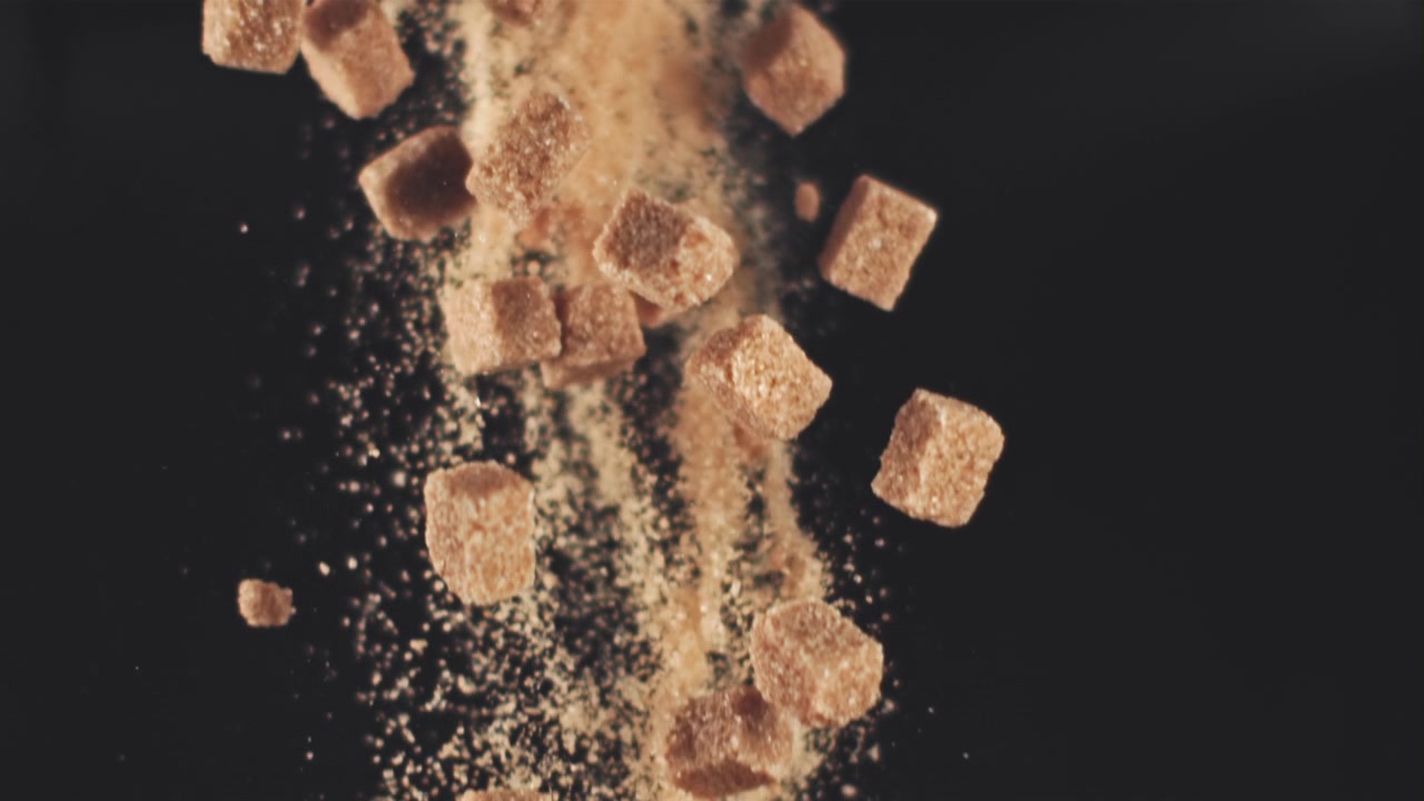 Slow Motion of Brown Sugar Cubes and Granules Falling on Black Background