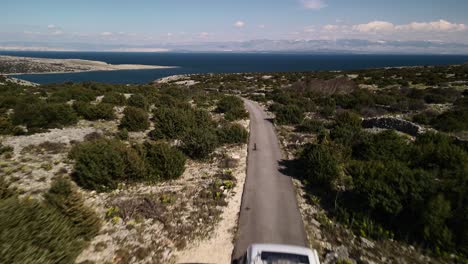 low altitude straight shot with drone flying over a van driving to the beach on a road surrounded by nature, croatia