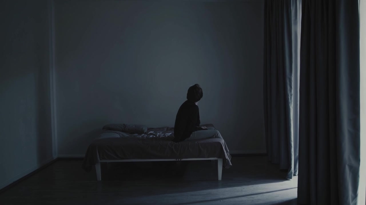 어둑한 방 침대에 혼자 앉아 있는 우울한 사람