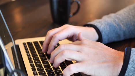 clip taken at coffee shop cafe of a caucasian man typing on computer keyboard then focus pulling to a coffee cup next to him