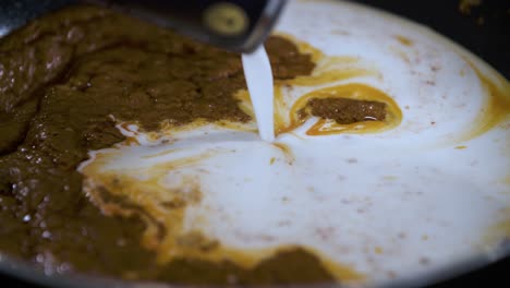 vertiendo lentamente leche de coco blanca de la lata en pasta de curry tailandés a fuego lento