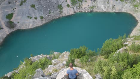 man standing on viewpoint looking at the famous blue lake near imotski in southern croatia