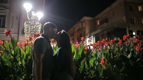 a romantic kiss between a couple at night in a city with flowers