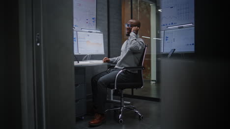 advanced trading office: excited financial analyst having phone call, celebrating profitable investments. african american businessman happy about successful financial deal or contract. vertical shot.