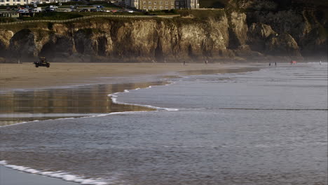 Golden-cliffs-in-background-with-sea-waters-rolling-over-reflective-beach-surface,-copy-space