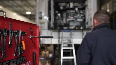 skilled mechanic choosing an wrench key from a red toolbox then climbing a leader after that procedes to work on a broken reefer traile