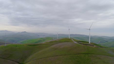 forward dolly approaching wind turbines atop a hill with distant smokey mountain mist at dusk