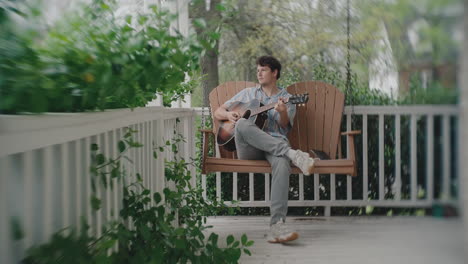 man playing guitar on a porch swing