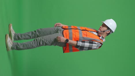 full body side view of asian male engineer with safety helmet having a headache while working in the green screen background studio