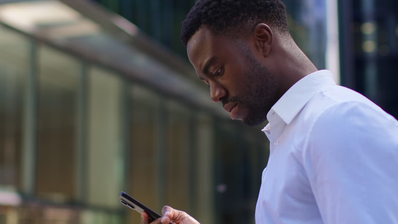 Young Businessman In Shirt Sleeves Looking At Mobile Phone Standing Outside Offices In The Financial District Of The City Of London UK