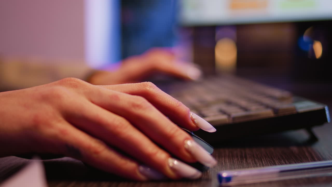 Close-up of a woman typing on a keyboard and using a computer mouse