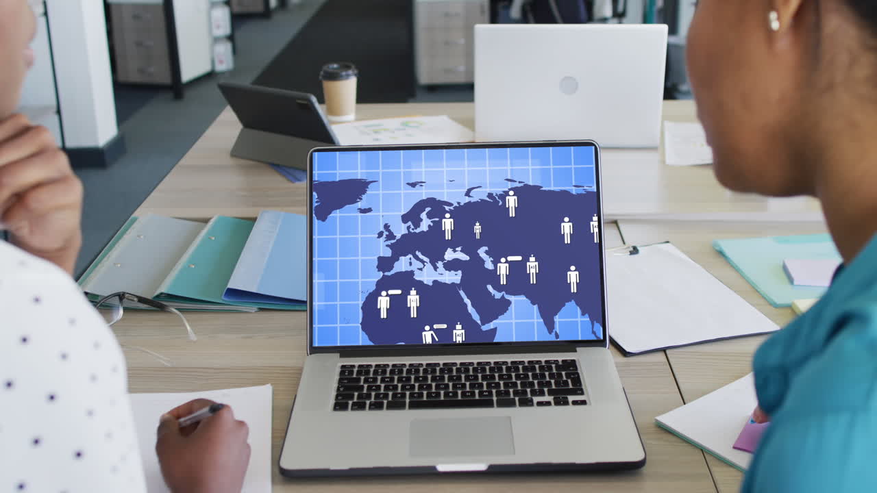 Diverse business people using laptop with digital world map and icons on screen in office