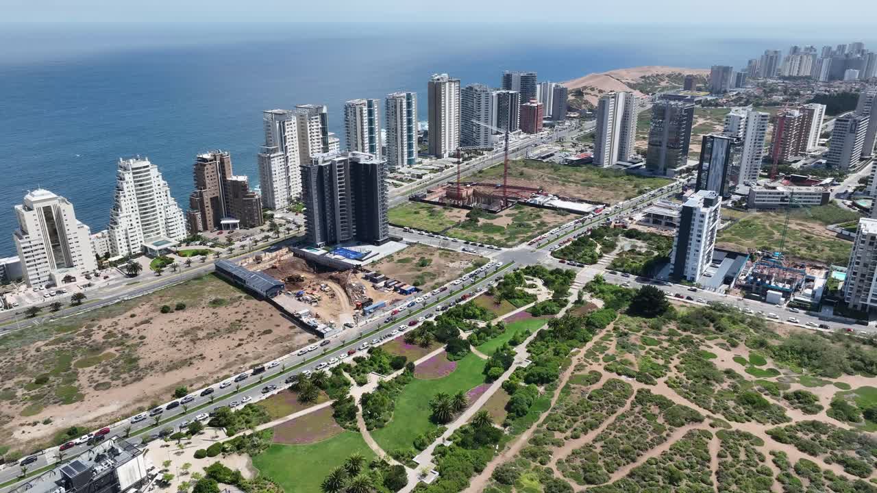 Tilting down drone aerial of Viña del Mar coastal towers, highway with traffic, parks, and Pacific Ocean with sand dunes panorama, Chile