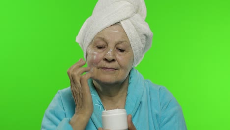 abuela anciana en bata de baño. anciana aplicando crema hidratante en la cara