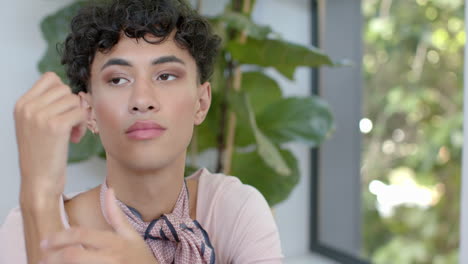 looking thoughtful, non binary person sitting at home with plants in background