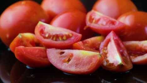tomates cerezos enteros y cuartizados contra un fondo negro con reflejo de agua