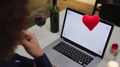 animation of heart over biracial man drinking wine and using laptop with copy space