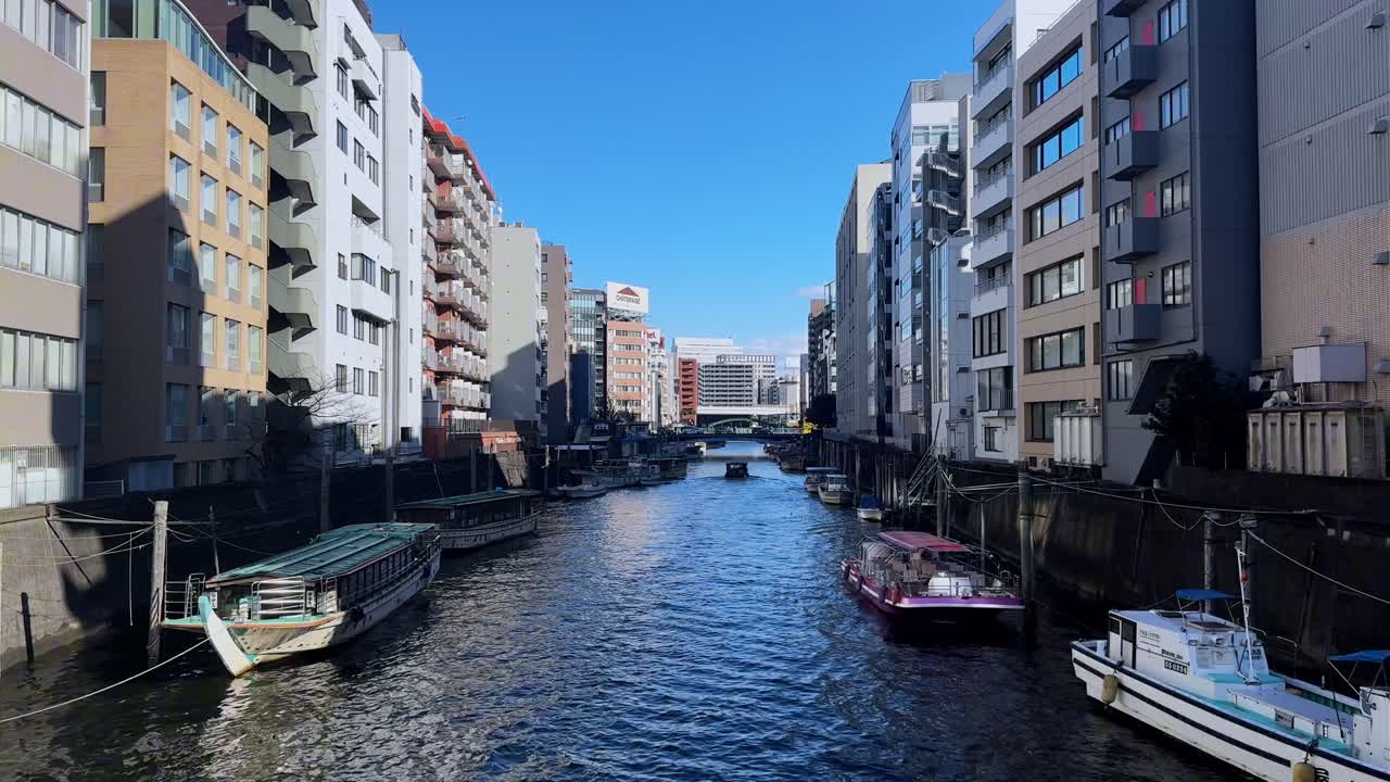 Waterway in Tokyo lined with modern buildings and moored boats under a clear blue sky