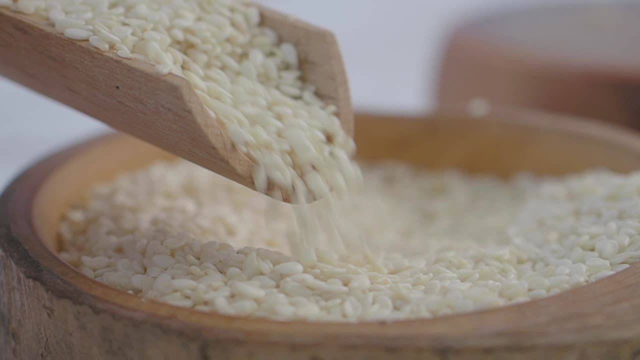 Sesame Seeds Pouring into Wooden Bowl