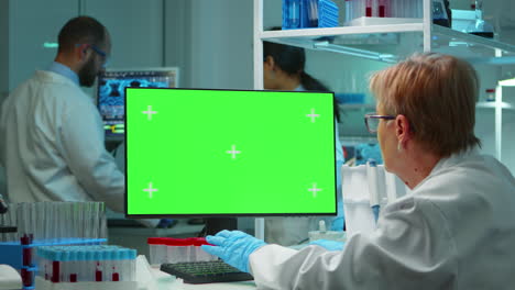 médico sénior trabajando en una computadora con pantalla verde