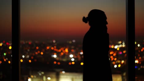 man is on the phone in a dark room, walking forth and back against window