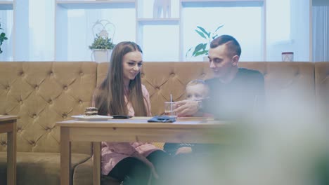 una joven familia feliz se sienta en un sofá de restaurante de cuero marrón