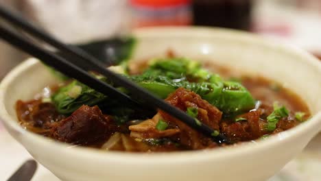 chopsticks lifting noodles with meat and greens