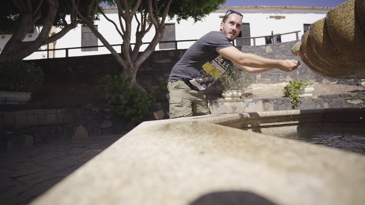 Joven aventurero viajero bebiendo agua fresca y fría de una fuente pública en Fuerteventura, Islas Canarias, España
